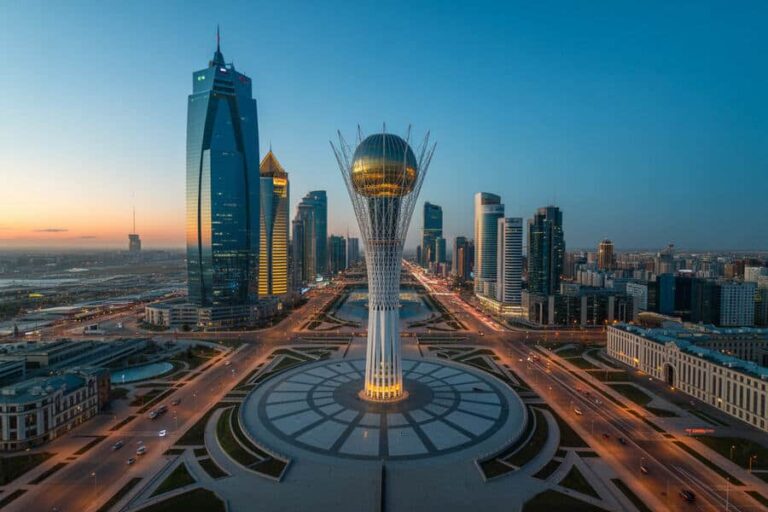 Aerial view of a modern city with a central Bayterek Tower surrounded by a circular plaza and tall skyscrapers at dusk in Astana, Kazakhstan.