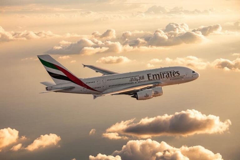 Emirates commercial airplane in midflight above orange clouds at sunset.