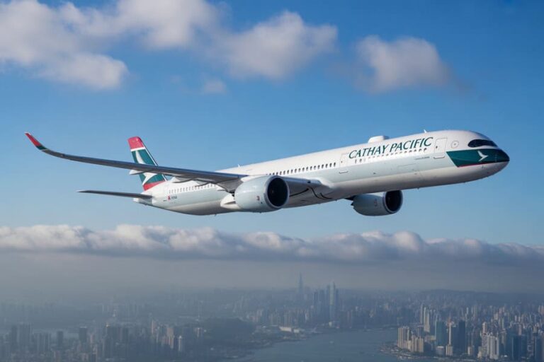 Cathay Pacific passenger airplane flying above a city skyline with blue sky and clouds