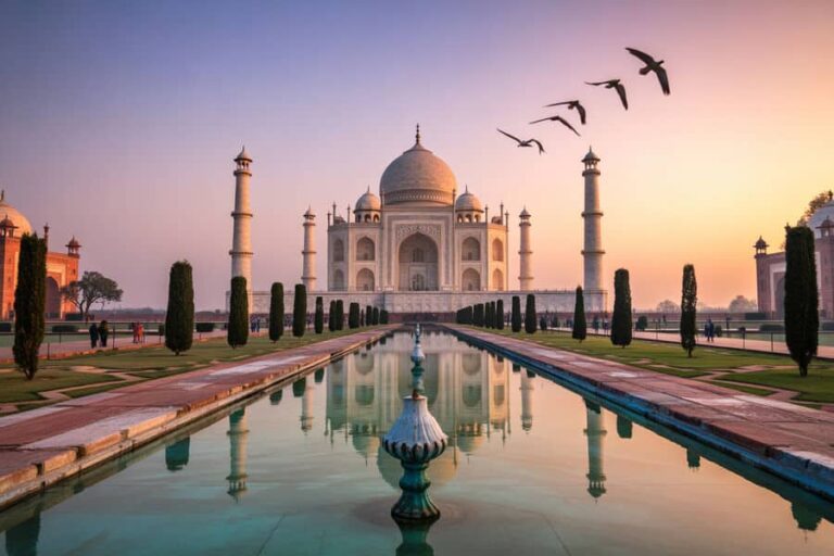 Taj Mahal at sunset with a pink‑orange sky, reflected in the long pool flanked by trees and pathways.