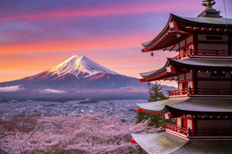Snow-capped Mount Fuji overlooking a sea of cherry blossoms with a red multi-tier pagoda in the foreground at sunset.