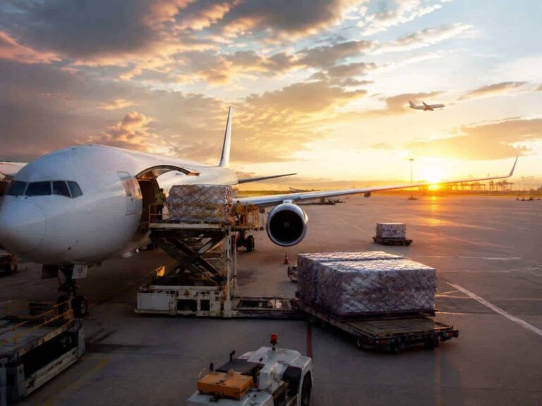 Airplane at the gate being loaded with cargo pallets at sunset on the tarmac at an airport