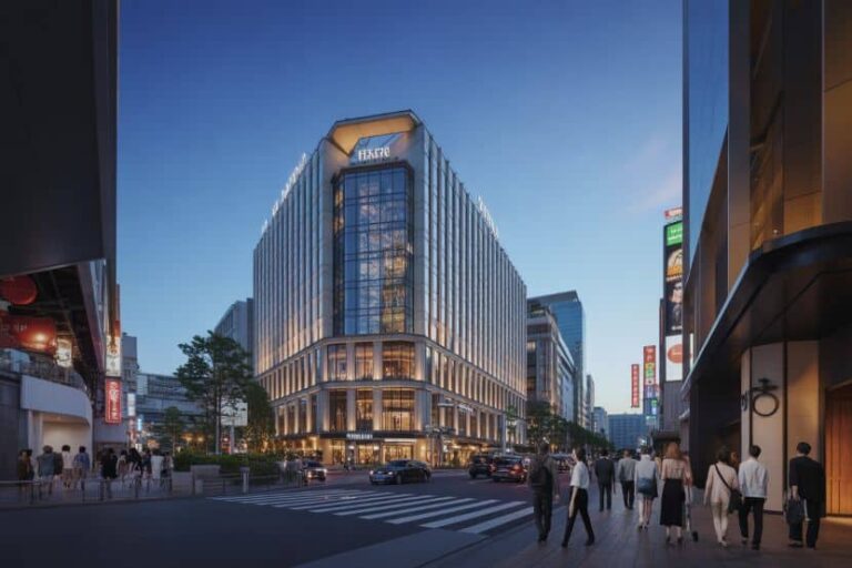 Large modern glass building at a busy city intersection at dusk, with pedestrians crossing and cars driving by.