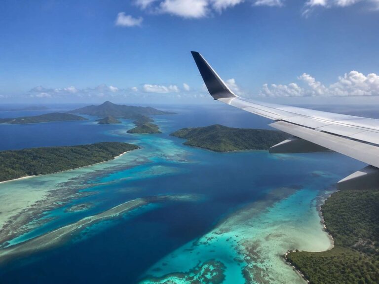 Aerial view of turquoise coral seas and green islands seen from an airplane wing over the ocean.