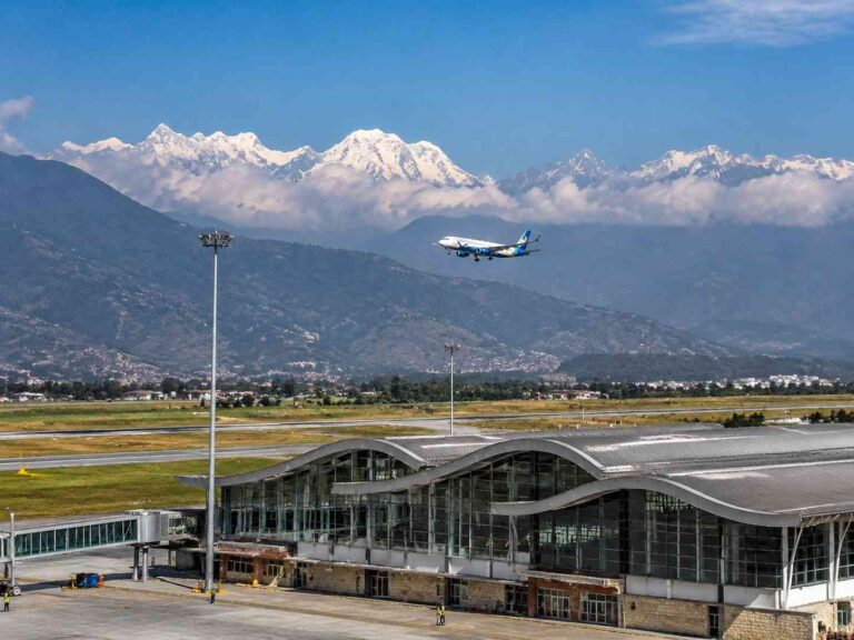 Airplane descending for landing at a modern airport terminal with snow-capped mountains in the distance.