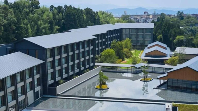 Aerial view of a modern campus with dark gray buildings, a central courtyard, and a reflective water feature.