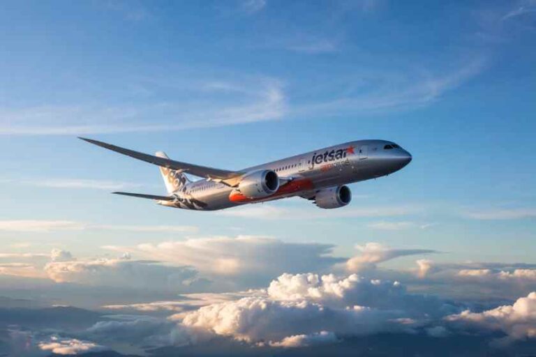 Jetstar passenger jet flying above white clouds in a blue sky