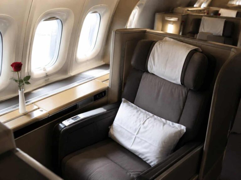 Premium airplane seat by a window with a white vase holding a red rose on the sill. (informative)