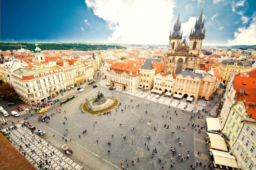 Aerial view of Prague's Old Town Square with a central fountain and the Church of Our Lady before Týn rising above colorful historic buildings in the background, viewed from above.