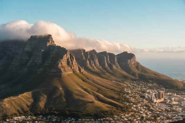 Table Mountain rises over Cape Town with clouds at the summit and the city and coastline below.