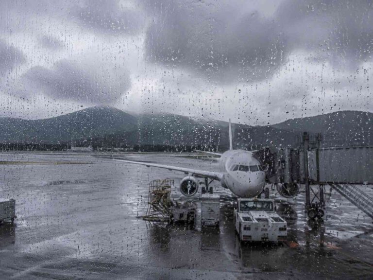 Airplane docked at a gate on a rainy tarmac, viewed through a rain-splattered window.
