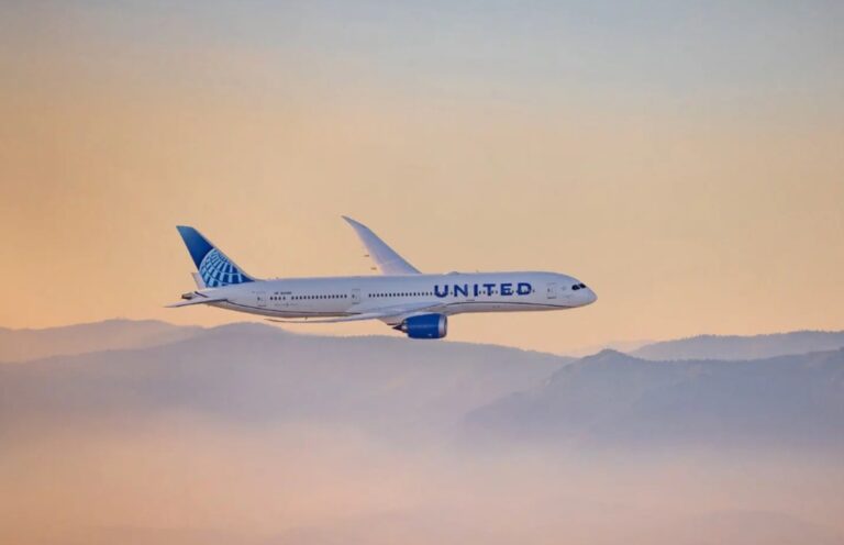 United Airlines passenger jet in flight above orange-tinged clouds with mountains in the distance.